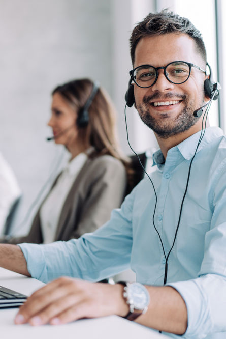 Man talar i telefon med hörlurar och har tangentbord och datorskärm framför sig i ett kontorslandskap med flera medarbetare..