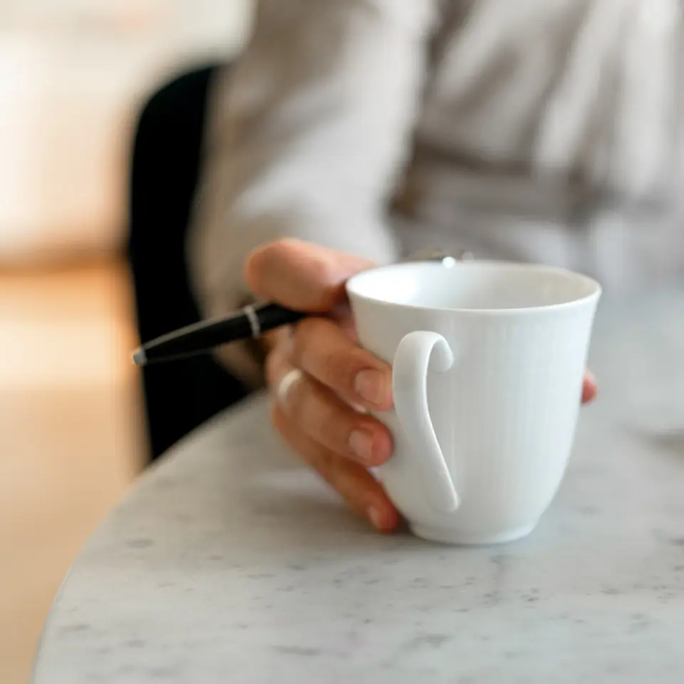 Person håller i en kaffekopp framför en dator.