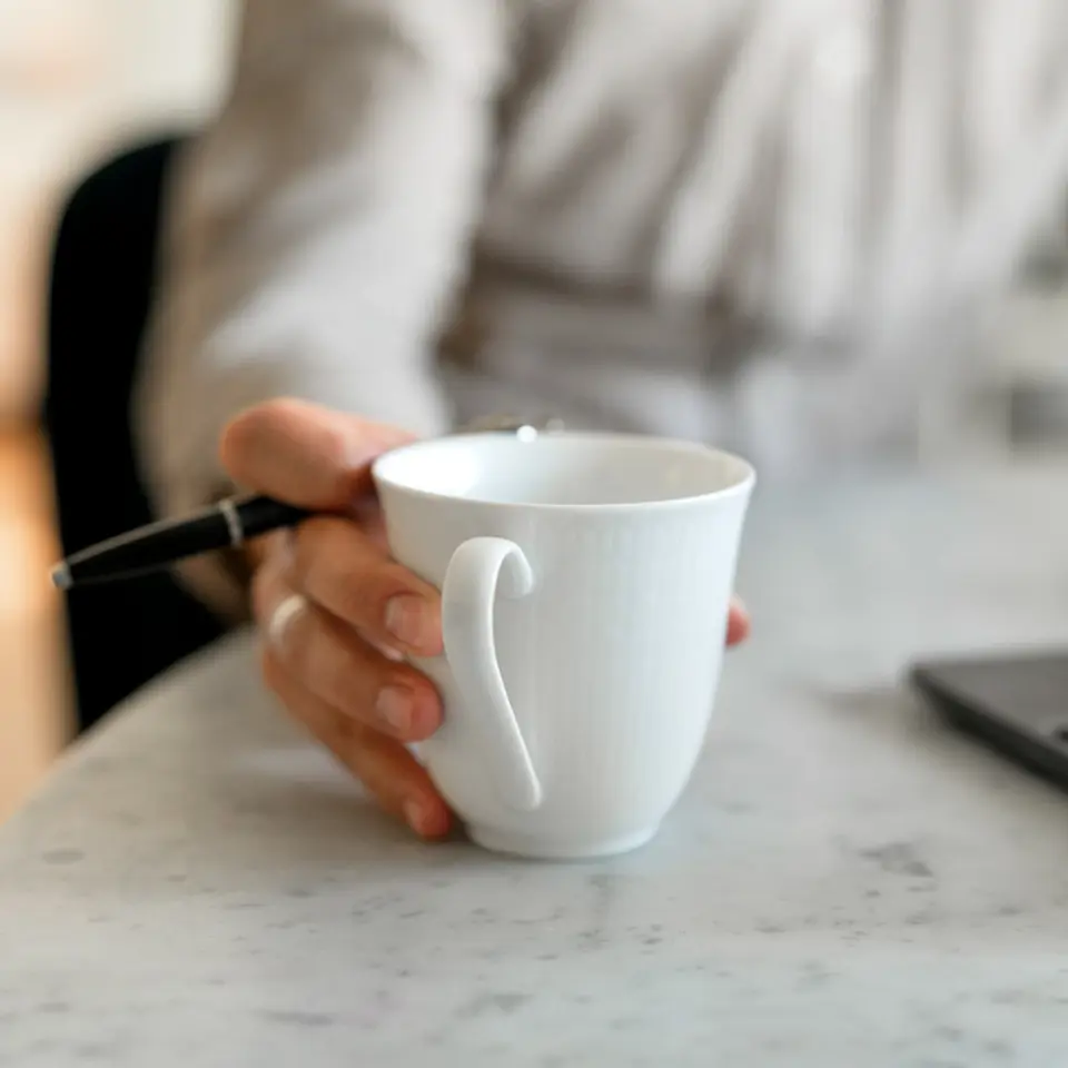 Person håller i en kaffekopp framför en dator.
