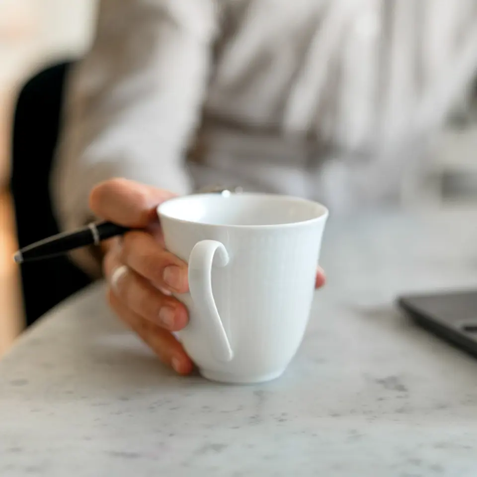 Person håller i en kaffekopp framför en dator.