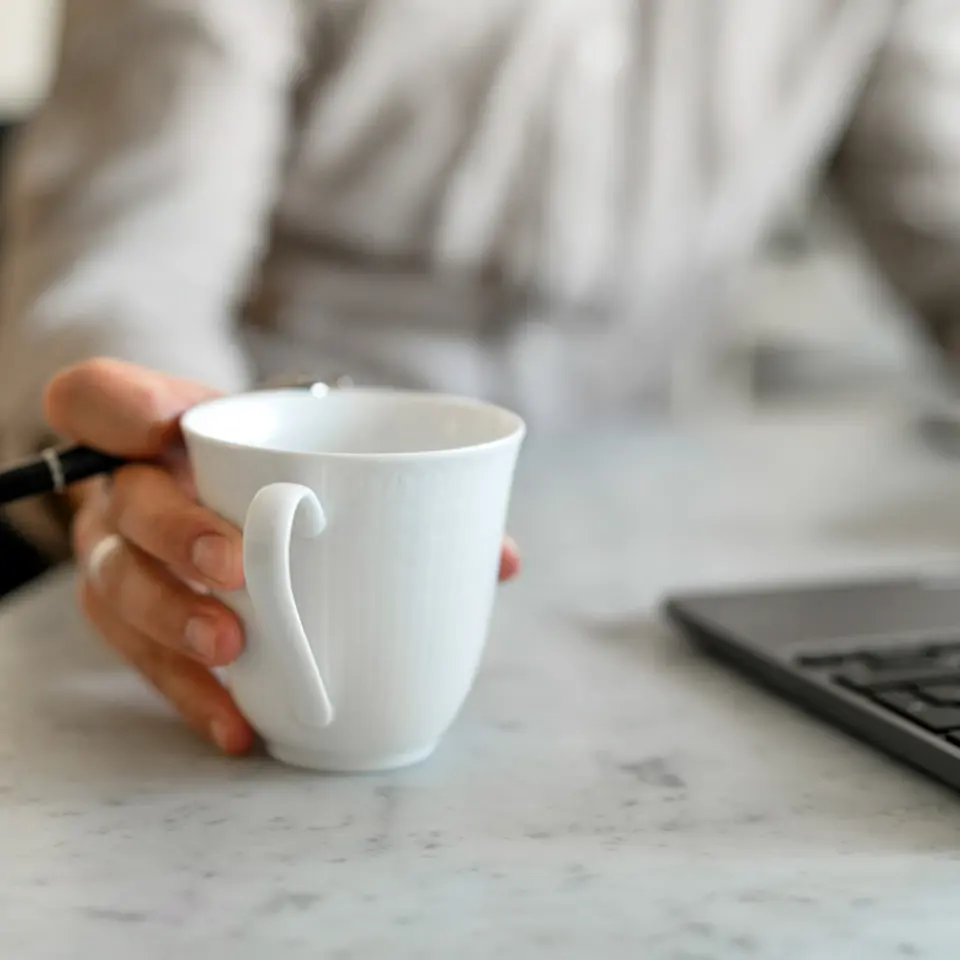 Person håller i en kaffekopp framför en dator.