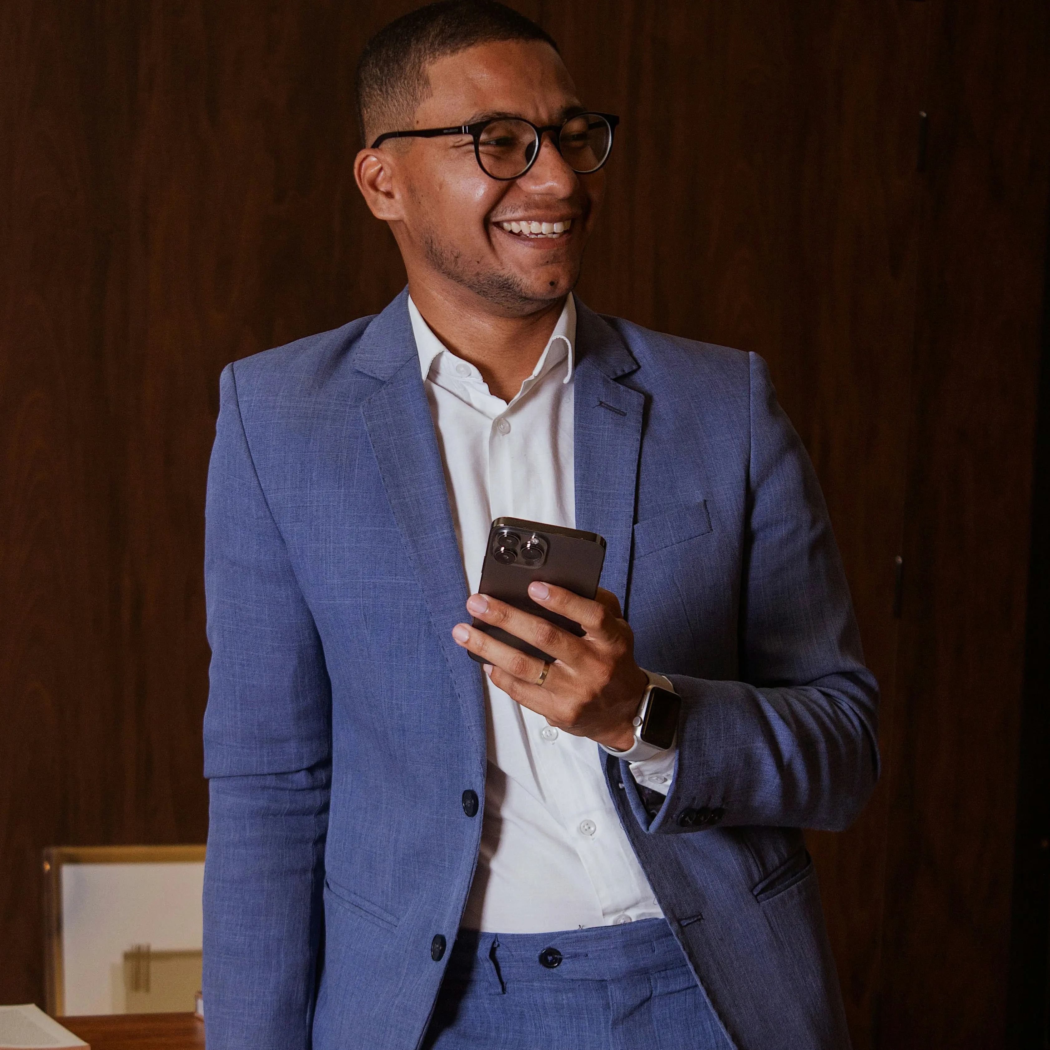 Man i blå kostym och glasögon står mot ett bord och håller i en mobil