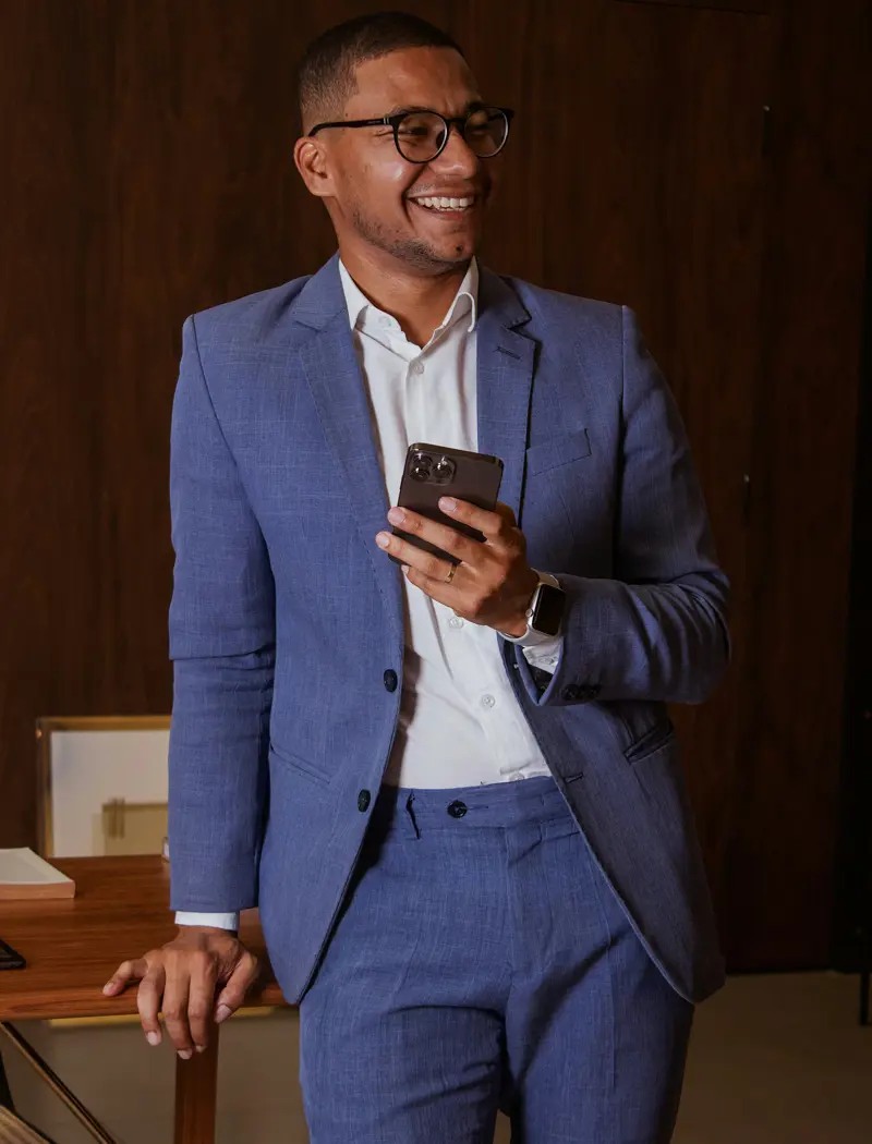 Man i blå kostym och glasögon står mot ett bord och håller i en mobil