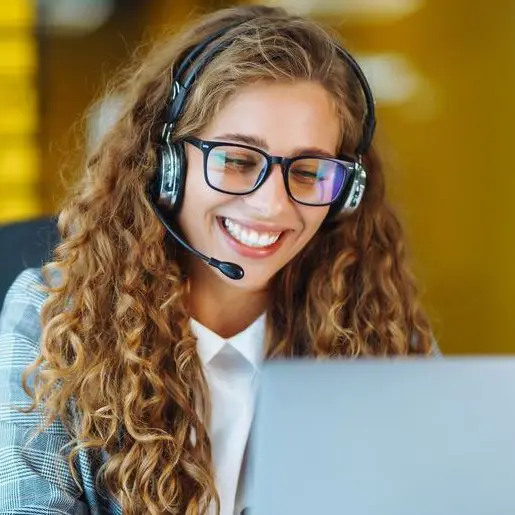 kvinna i kontorslandskap talar i telefon via ett headset med datorskärm framför sig.