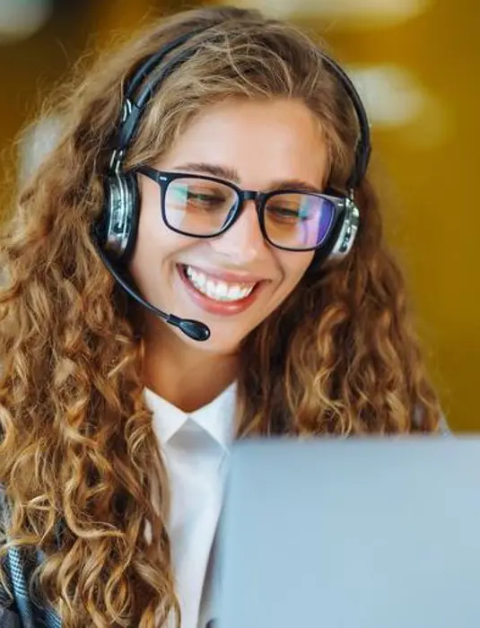 kvinna i kontorslandskap talar i telefon via ett headset med datorskärm framför sig.