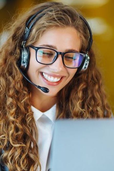 kvinna i kontorslandskap talar i telefon via ett headset med datorskärm framför sig.